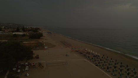 drone image of beachfront hotels and neatly arranged beach umbrellas on a quiet sandy shore near rethimno, crete, greece under a cloudy sky during twilight