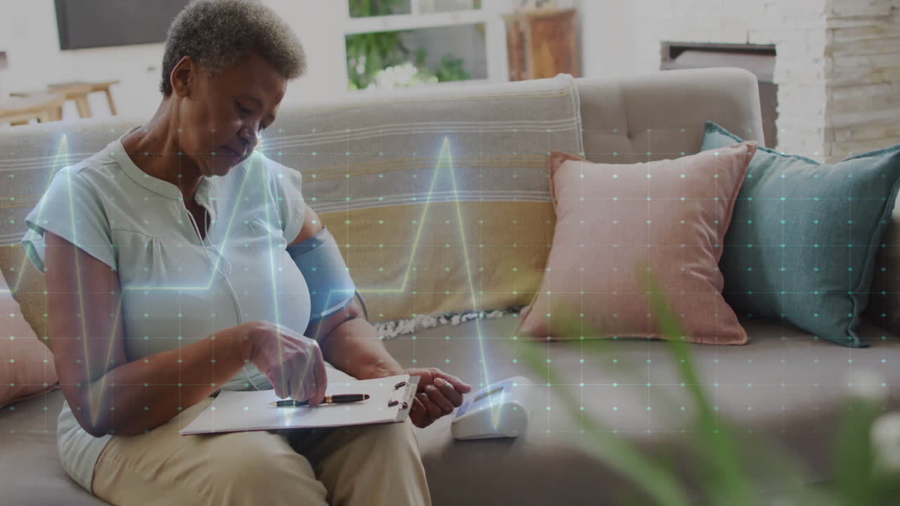 Animation of cardiograph over senior biracial woman taking notes on clipboard