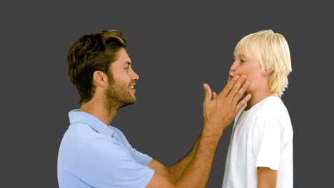 Man-pressing-inflated-cheeks-of-his-son-on-grey-background