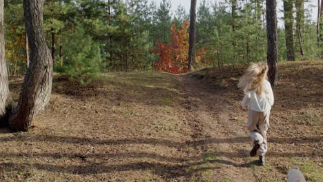 a teenage girl runs with a dog along a path in a pine forest.