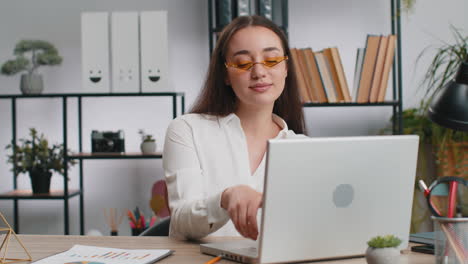 mujer de negocios caucásica con auriculares escuchando música bailando después de trabajar en una computadora portátil en la oficina