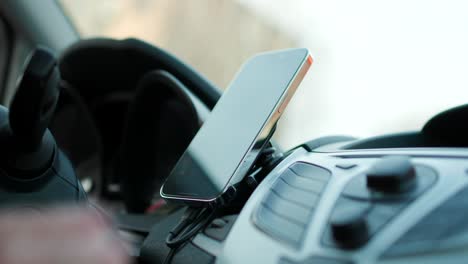 close up shot of mounting smartphone on magnetic dashboard holder beside steering wheel inside car