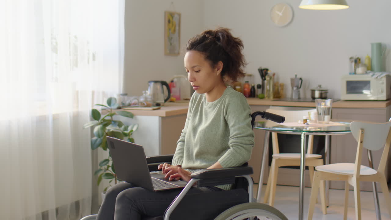 Donna che usa il laptop in sedia a rotelle a casa.