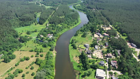 aerial: high altitude flight over river bank with forest and houses on each side of river