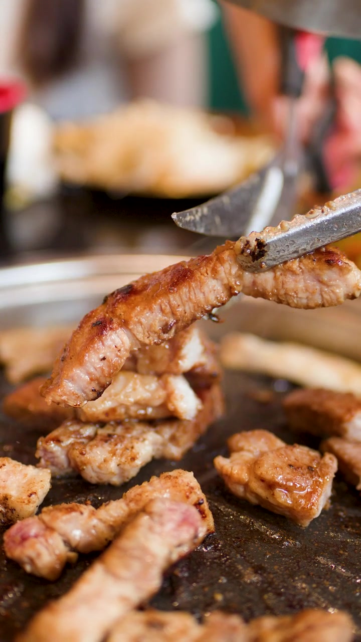 Una mano usa pinze e forbici per tagliare carne di maiale alla griglia su una griglia per barbecue coreano