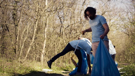 joven voluntario haciendo limpieza de basura con una larga garra para agarrar la basura
