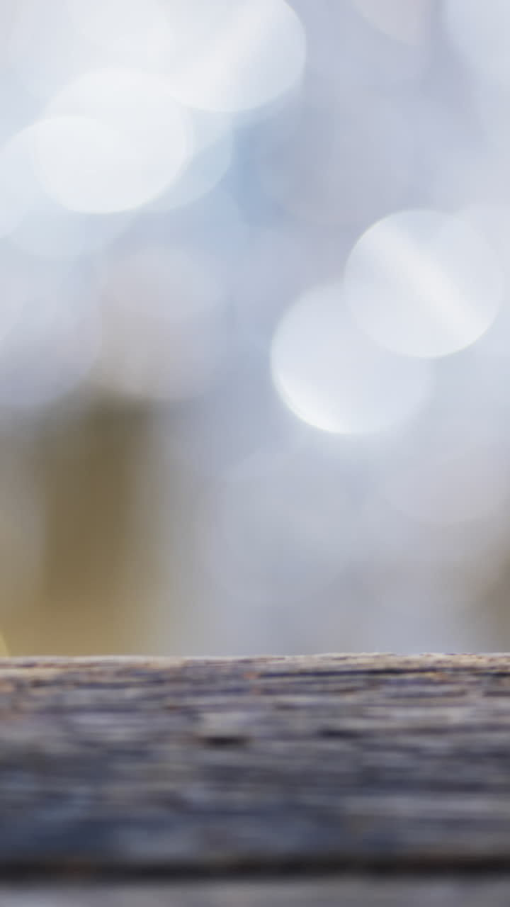 Vertical video of flickering white bokeh spots of light with copy space and wooden surface