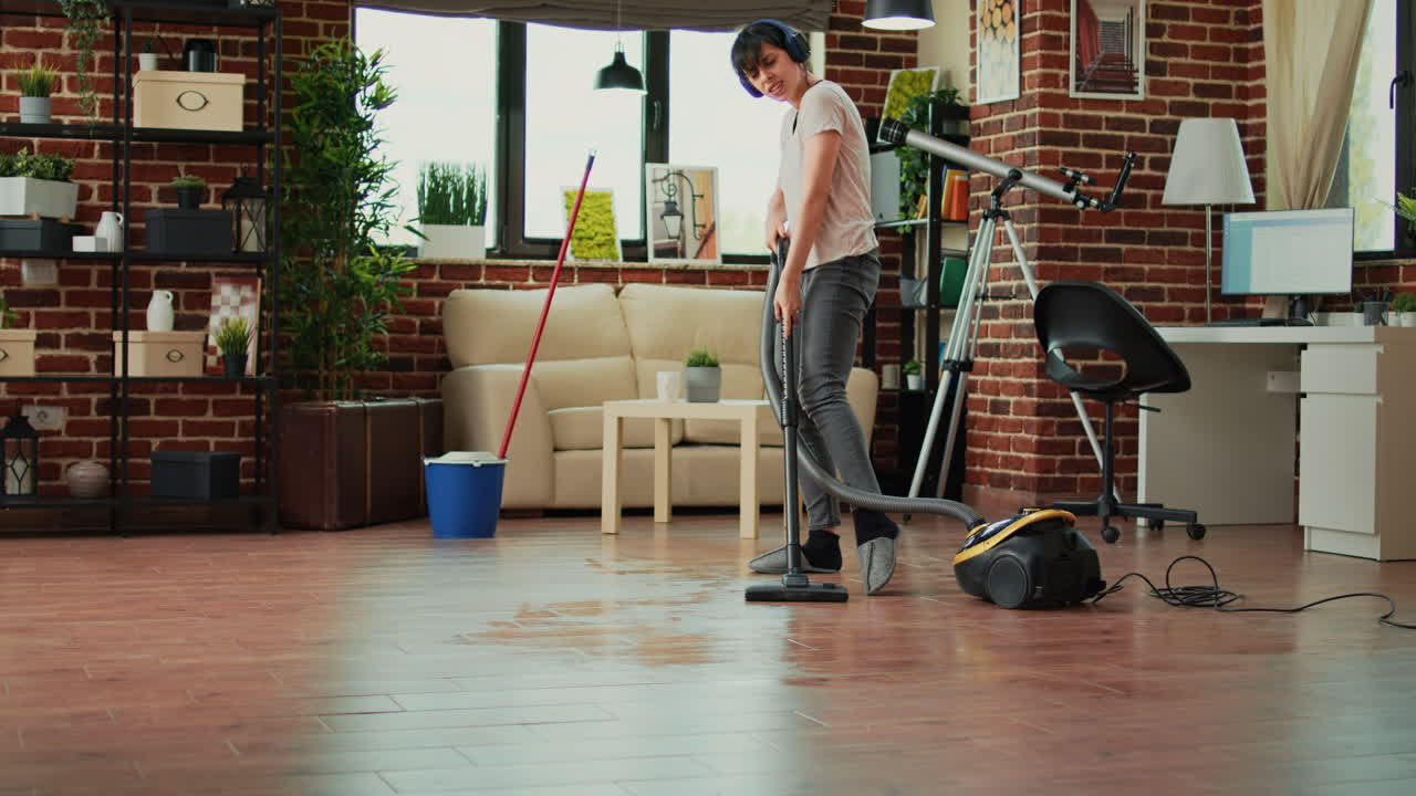 Female adult listening to music on headset and vacuuming floors at home