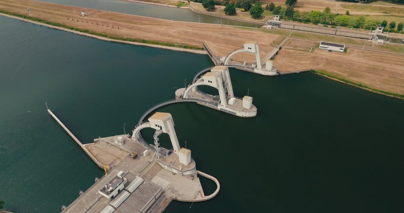 High-altitude drone orbit above a hydraulic hydroelectric power plant in a Dutch canal, revealing renewable energy infrastructure surrounded by waterways and countryside.