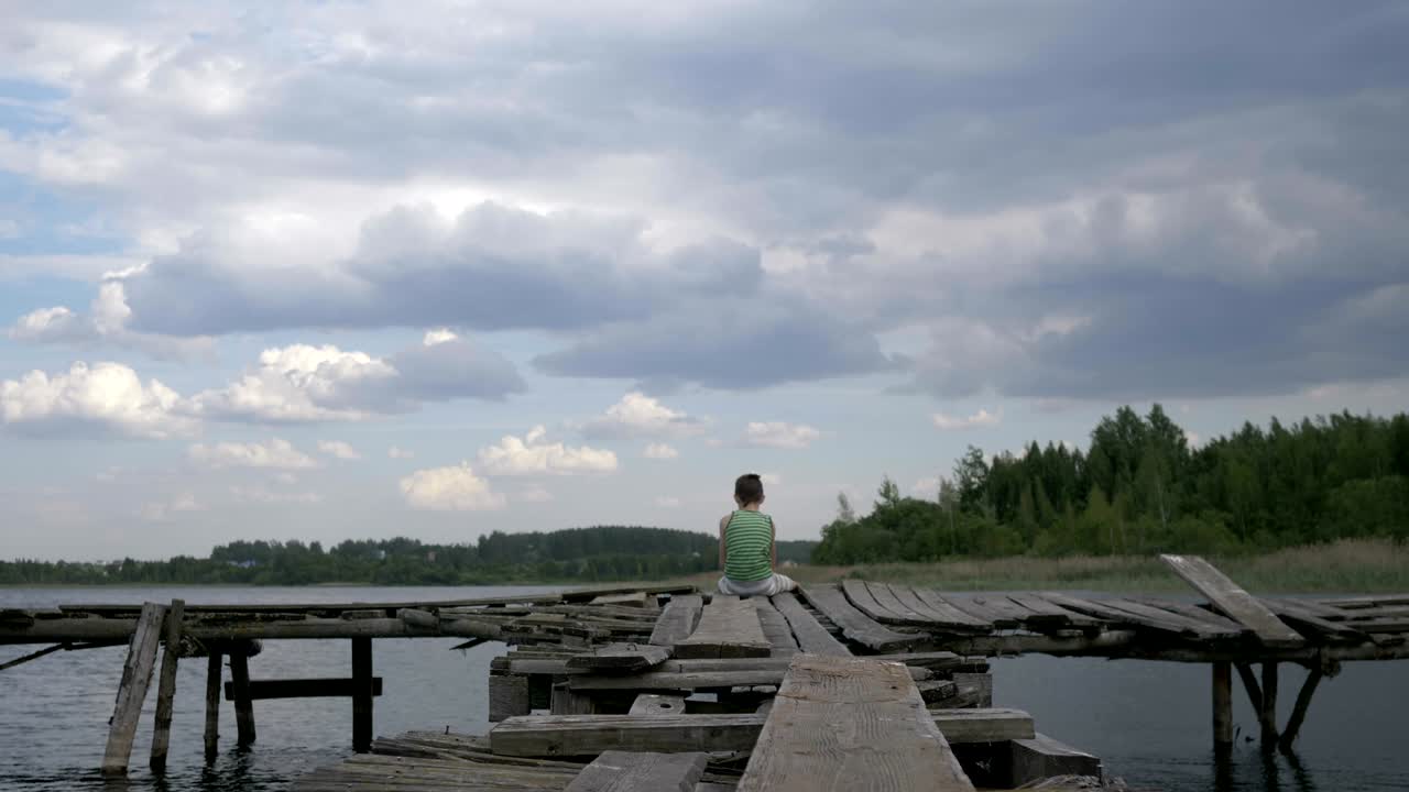 lonely boy sits on the edge of the pier in windy rainy weather, depression, thoughts about life, outdoors