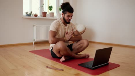 bearded man talk on video call sit on yoga mat greets in namaste