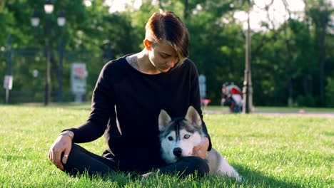 beautiful young woman playing with funny husky dog outdoors in park