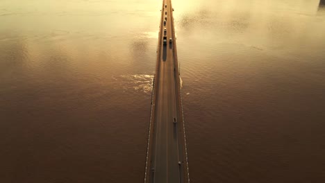 symmetrical birdseye view of cars traveling on a road bridge over river mekong during golden hour