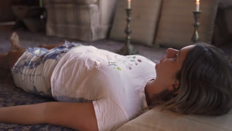 4k young latin female meditating ritual with candles lying on the floor in a wooden home