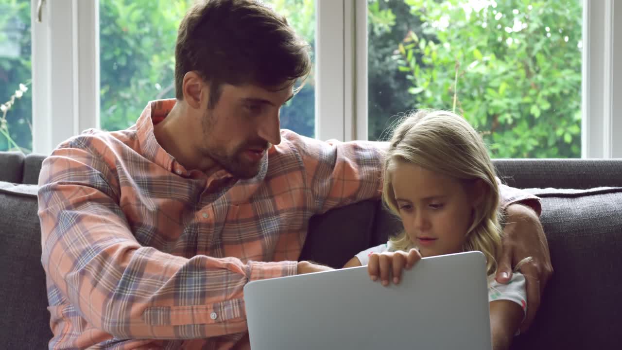 padre e hija usando computadora portátil en el sofá en casa 4k