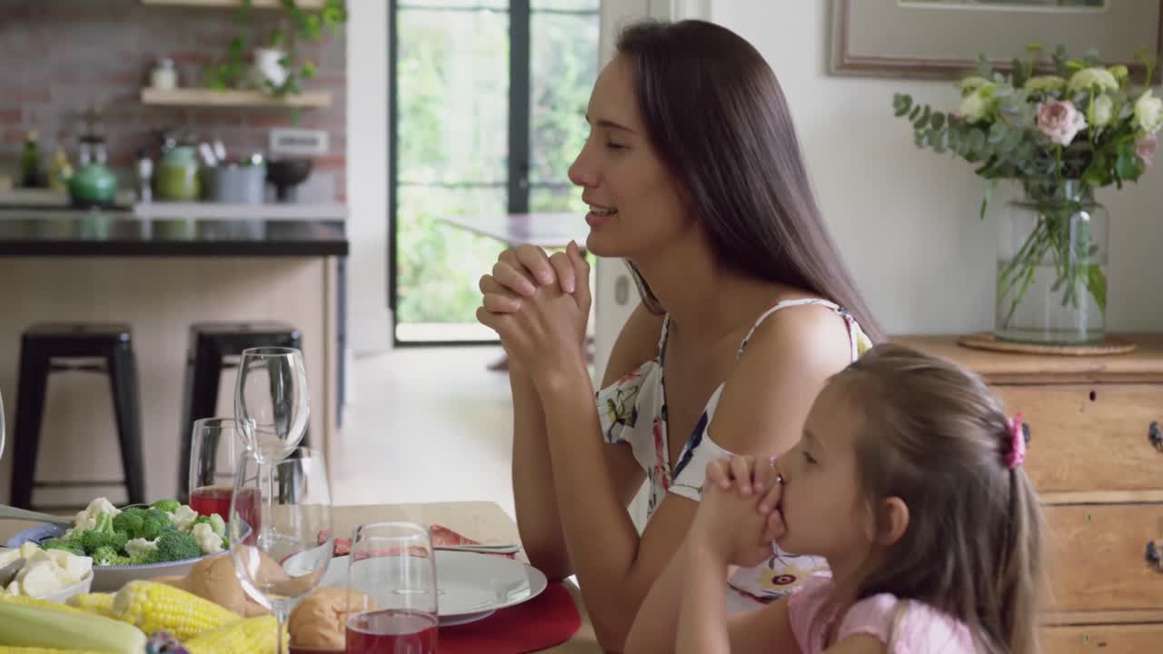 madre e hija orando antes de comer en la mesa de comedor 4k
