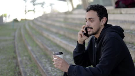 Cheerful-man-with-coffee-to-go-talking-by-smartphone