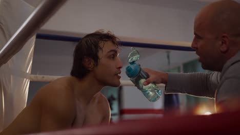 entrenador caucásico dando agua al atleta caucásico en el ring de boxeo