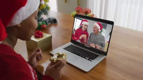 African-american-woman-with-santa-hat-using-laptop-for-christmas-video-call-with-family-on-screen