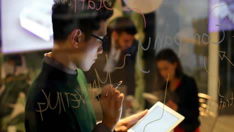 male executive writing on glass board while using digital tablet in office 4k