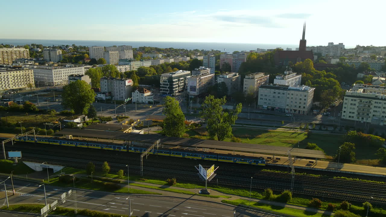 tren estacionado en la estación de tren maksymiliana con vistas a la torre de la iglesia parroquial de san antonio y su barrio en gdynia, voivodato de pomerania, polonia