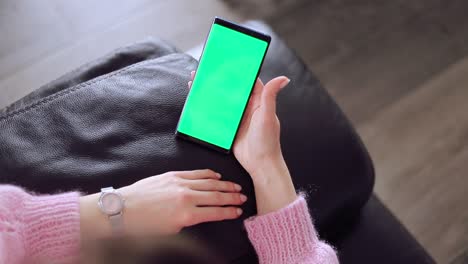 use green screen for copy space closeup. chroma key mock-up on smartphone in hand. woman holds mobile phone iphone and swipes photos or pictures left indoors of cozy home