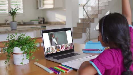 Schoolgirl using laptop for online lesson at home, with diverse teacher and class on screen