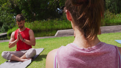 Rear-view-of-caucasian-female-instructor-practicing-yoga-with-diverse-group-in-park