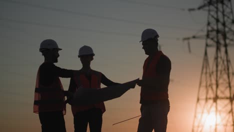 structure of power towers, young professional engineers are discussing project of electric plant backdrop of sunset, silhouette