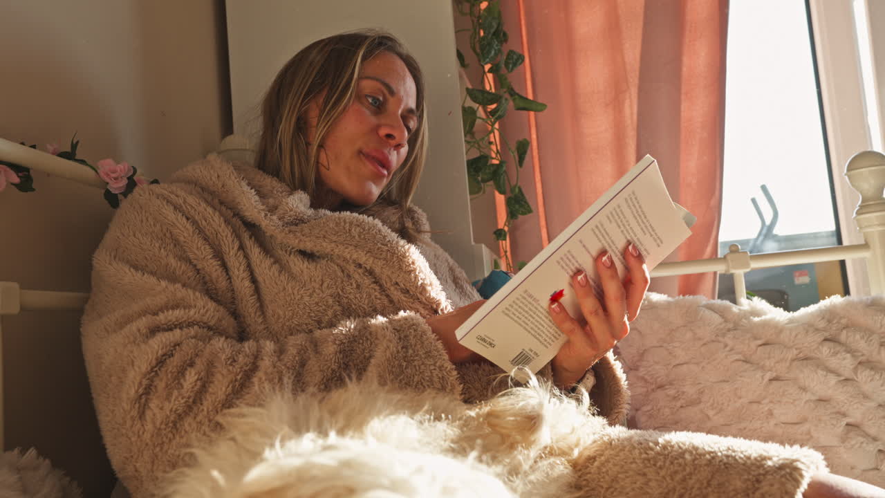 Nahaufnahme eines Porträts einer Frau, die bequem ein Buch liest, während sie im Bett liegt.