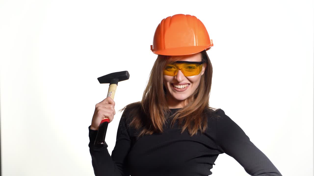 A pretty woman with orange helmet and eyeglasses is posing with a pickaxe in her hands on a white background in the studio. Profession of engineer
