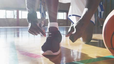 jugador de baloncesto afroamericano atando zapatos con el equipo en el fondo