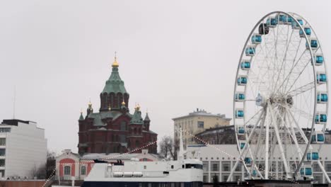 moving-view-with-perspective-of-the-Helsinki-ferris-wheel-upfront-and-the-uspenski-orthodox-cathedral-in-the-back,-seen-from-the-ferry-in-the-old-port
