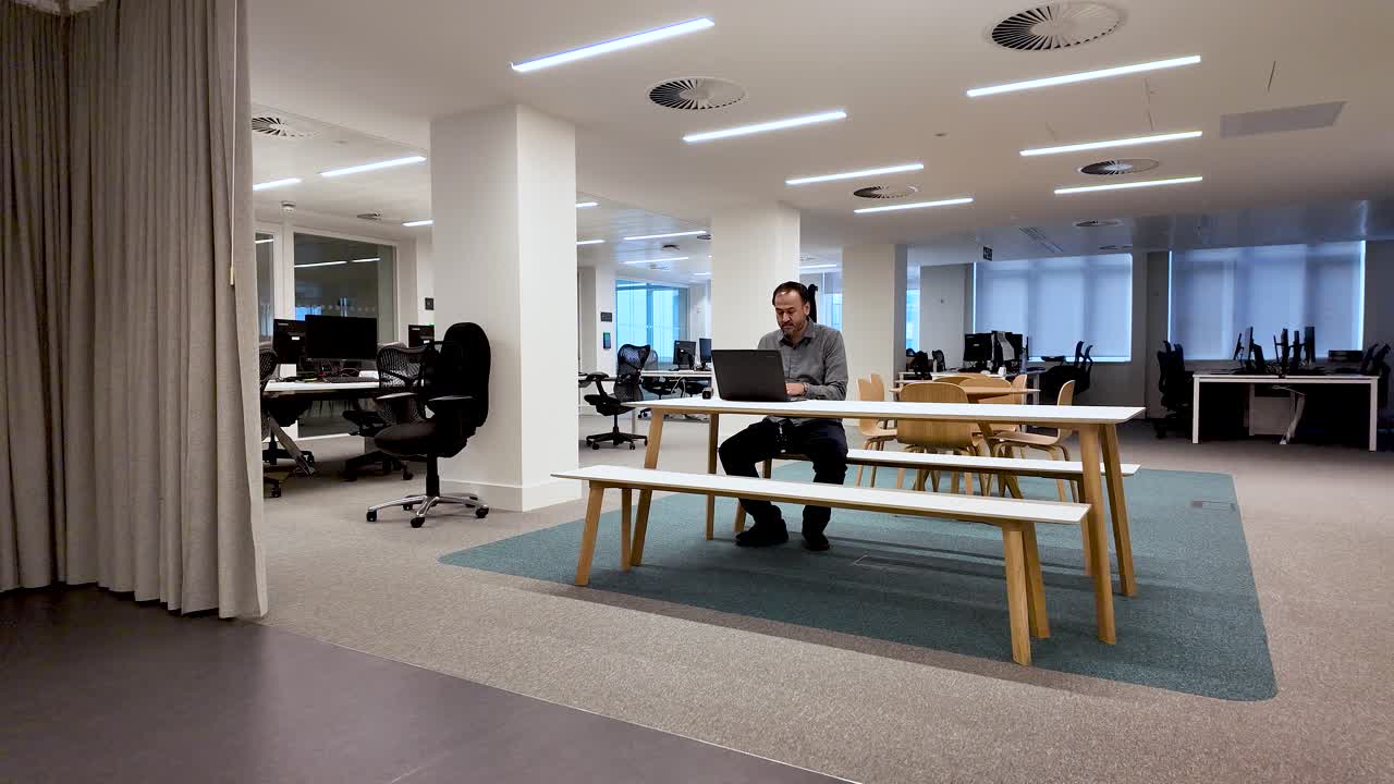 Remote work loneliness and isolation a South Asian man is working alone on a laptop at a long table