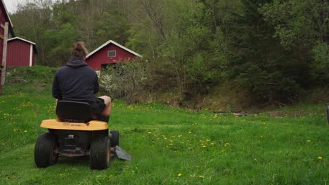 man riding mower, moxing grass outside the cabin