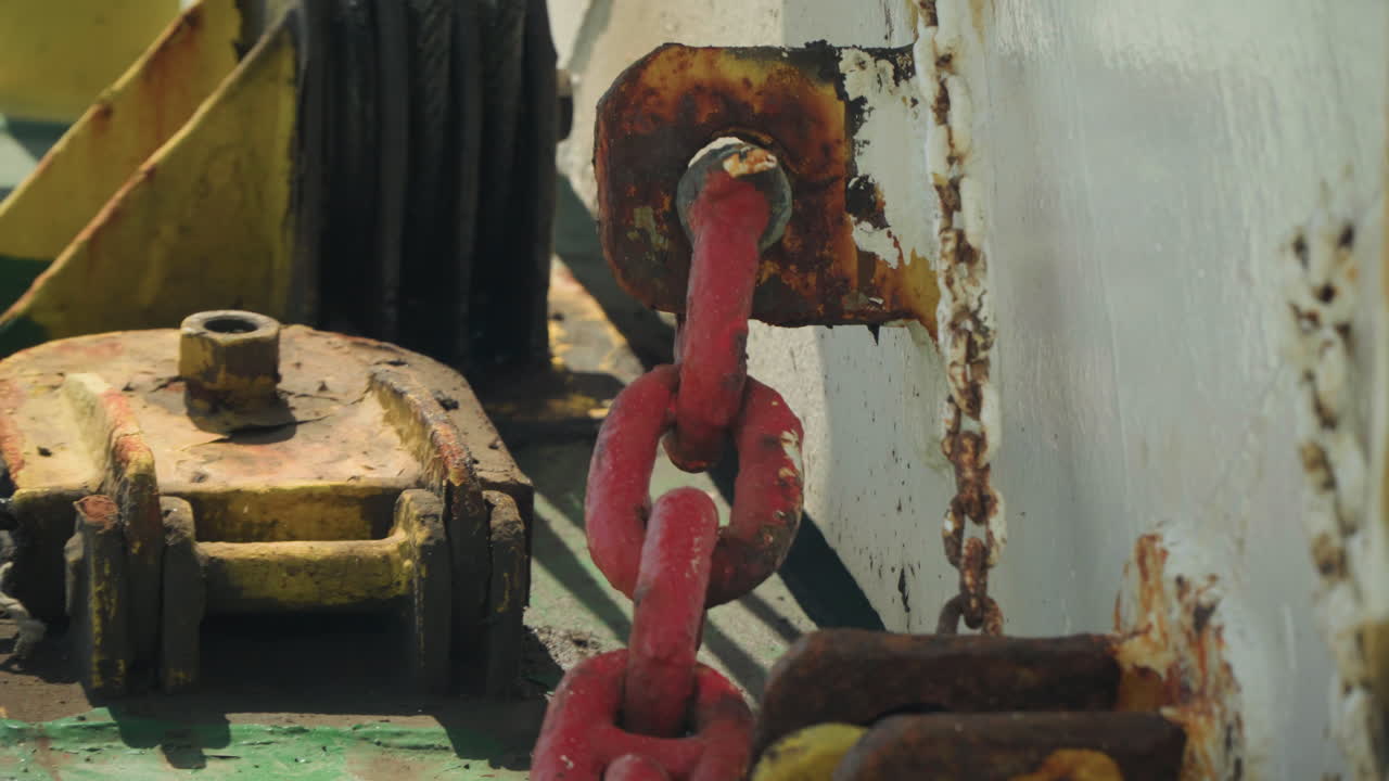 Catena rossa arrugginita sul ponte, primo piano di verricello e puleggia corrosa con vernice scrostata, bulloni ossidati, metallo invecchiato e texture industriali che suggeriscono ispezione del marinaio, manutenzione dell'attrezzatura, ambiente marino