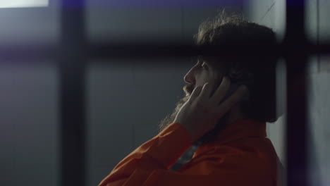 criminal in orange uniform talks on phone in prison cell