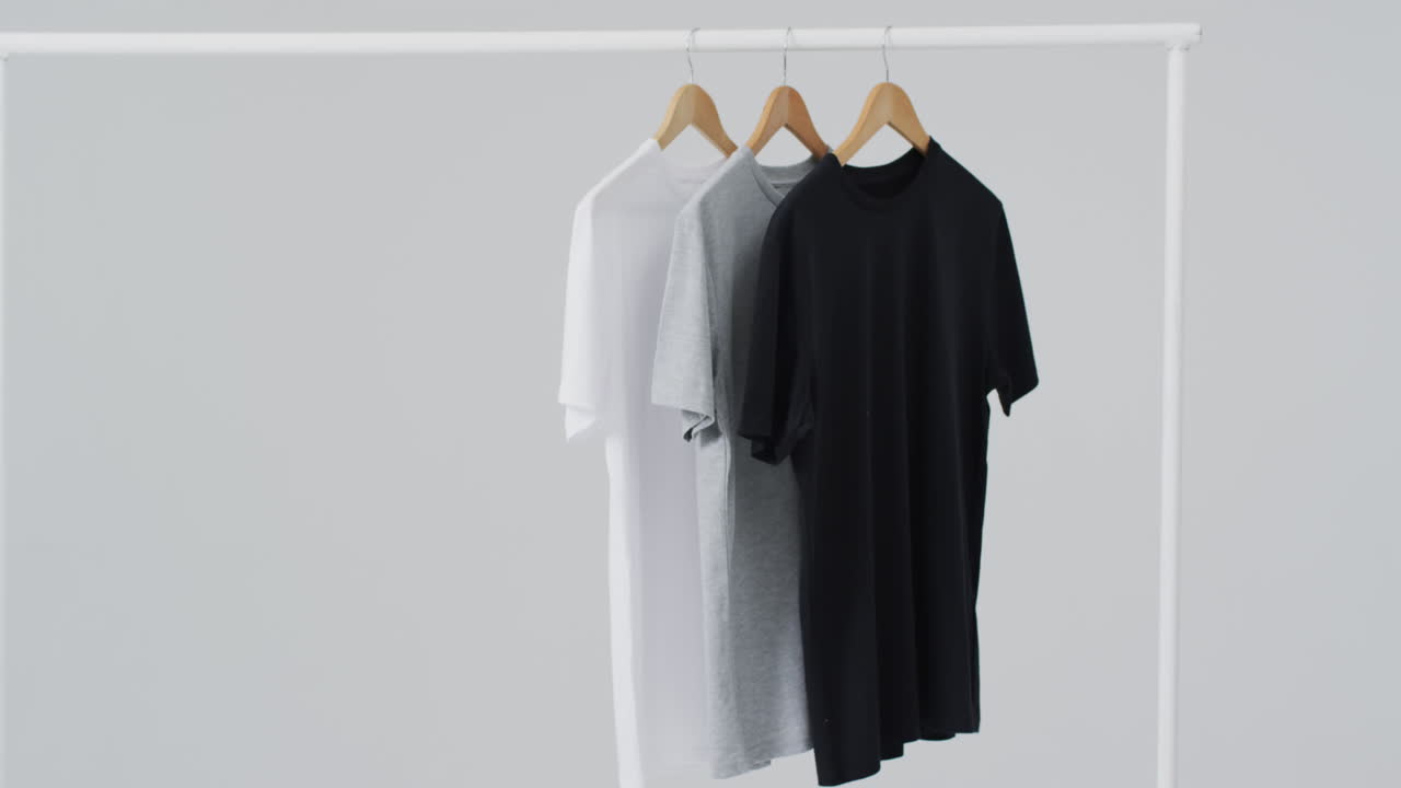 Video of white, grey, black t shirts on hangers and copy space on white background