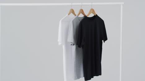 video de camisetas blancas, grises y negras en perchas y espacio de copia sobre fondo blanco