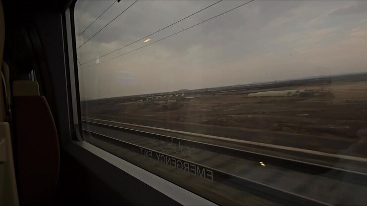Horizontal video train window glass view desert afternoon fast motion wide open empty land train track visible cloudy sky speed journey scenic desert view