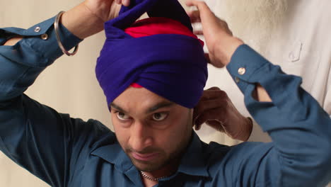 Close-Up-Studio-Shot-Of-Two-Sikh-Men-Tying-Fabric-For-Turban-Against-Plain-Background-3