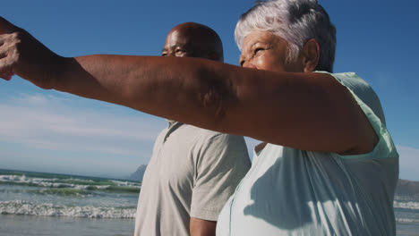 smiling senior african american couple walking and holding hands at the beach