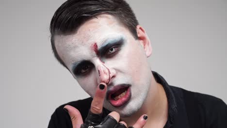 face painted man showing tongue and devil horns fingers, closeup portrait, slowmo