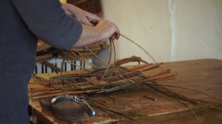 A basketmaker shapes and weaves together the wooden rods while making a traditional welsh basket by hand