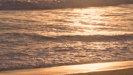 close up moving water waves hit the beach in the gold hour evening