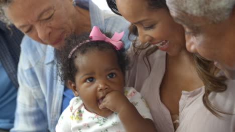 extended family sitting on sofa at home with baby daughter