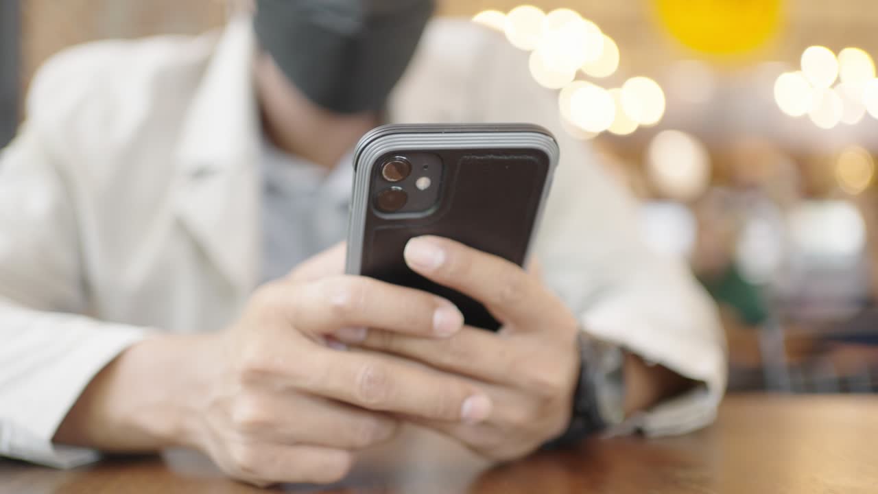 A young businessman wearing a surgical mask is taking a video conference with customers via a smart phone connected to the Internet.