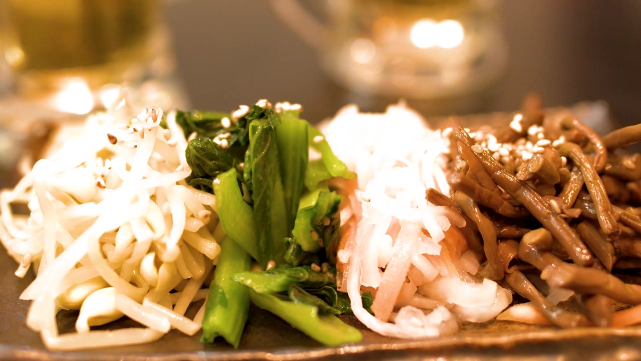 暖かく薄暗い和食レストランで、箸が皿から味付けされた野菜をつまみ上げる。