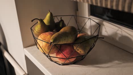 a black geometric bowl of pears and apples on a windowsill