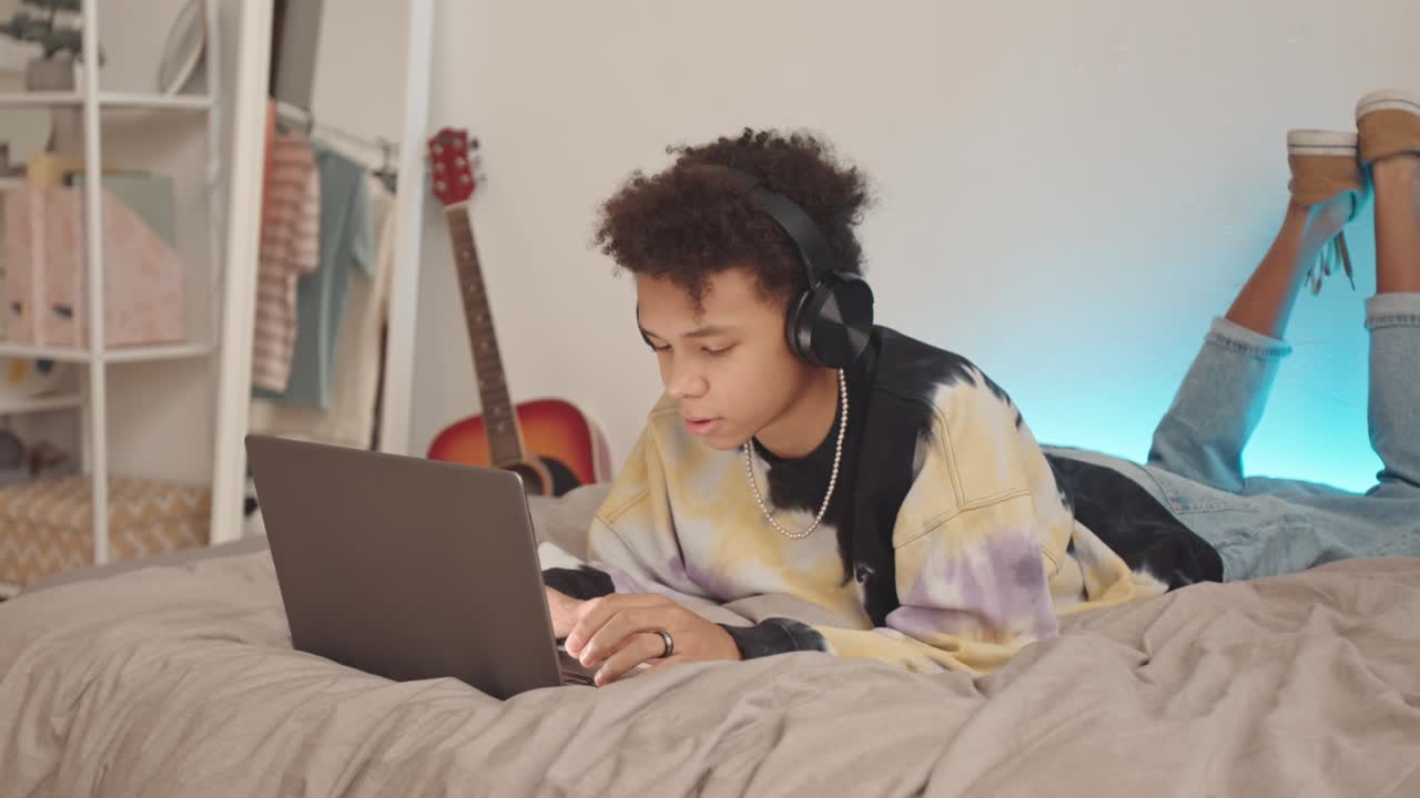 niño adolescente biracial con auriculares usando una computadora portátil en casa